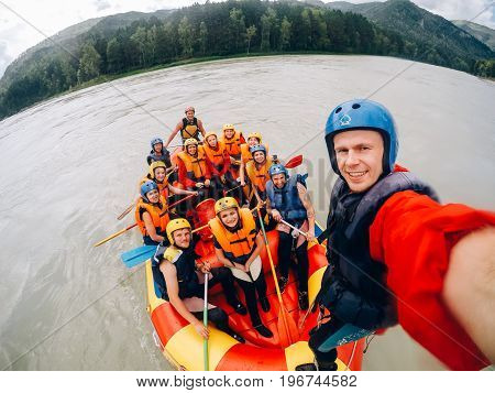 mountain Altai, RUSSIA - July 16, 2017: man in a helmet holds an action camera and makes selfie on the background of friends with oars, rafting