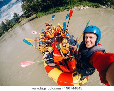 mountain Altai, RUSSIA - July 16, 2017: man in a helmet holds an action camera and makes selfie on the background of friends with oars, rafting