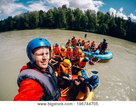 mountain Altai, RUSSIA - July 16, 2017: man in a helmet holds an action camera and makes selfie on the background of friends with oars, rafting