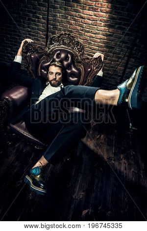 Portrait of a stylish handsome man on a vintage armchair. Fashion shot. Men's clothing and accessories.