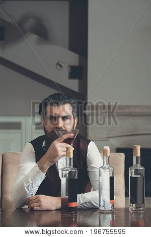 Hipster drinking red wine alone in restaurant. Brutal man with beard sitting at table with three bottles and glass. Alcohol abuse. Addictive and convive. Unhealthy lifestyle and bad habits