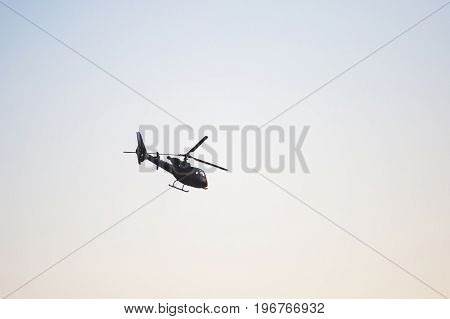 A flying black helicopter aircraft during the flight with blue sky in the background