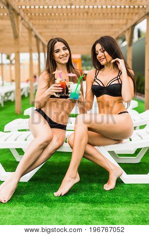 Two Beautiful Sexy Women In Bikini Drinking A Cocktails While Relaxing In The Swimming Pool. Summer