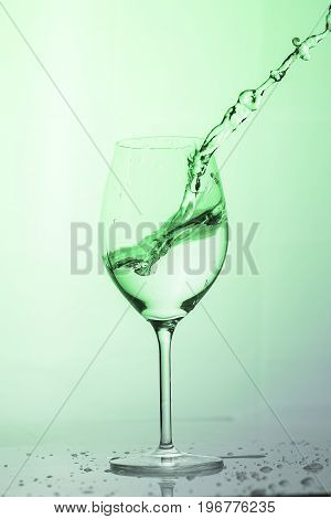 Water splashing out of a tall wine glass in color