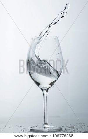 Water splashing out of a tall wine glass in color