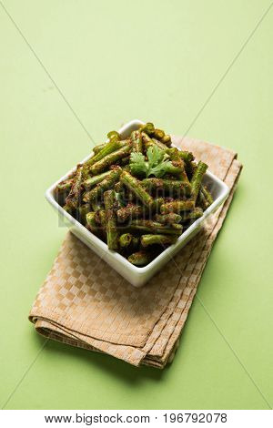 A Masala or fried vegetable dish consisting of green beans, onions, and curry spices, served in square bowl, selective focus