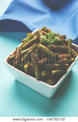 A Masala or fried vegetable dish consisting of green beans, onions, and curry spices, served in square bowl, selective focus