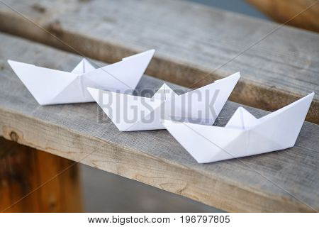 Three white paper boats on wooden bench closeup