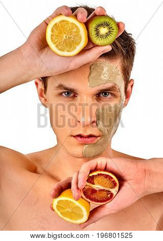 Facial mask from fresh fruits and clay for man concept. Face with treatment mud applied. Male holding lemon half for skin care procedure in salon. Cosmetic masks with natural ingredients.