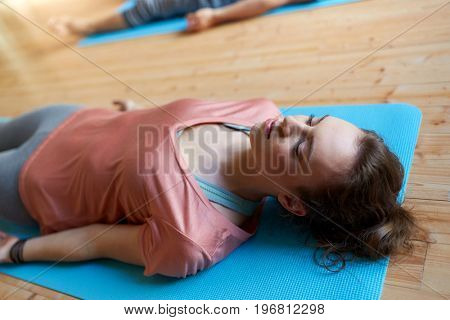 fitness, sport and healthy lifestyle concept - woman doing yoga corpse pose on mats at studio