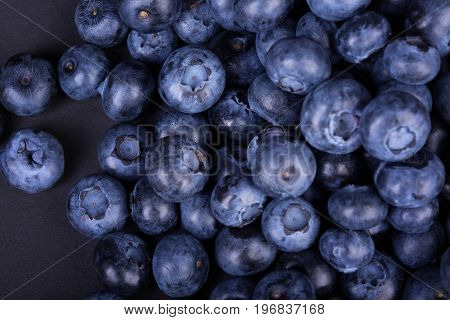 A macro picture of dark purple blueberries on a black background. Delicious and raw blueberries full of nutrients. Ingredients for light summer snacks. A group of freshly picked blueberries.