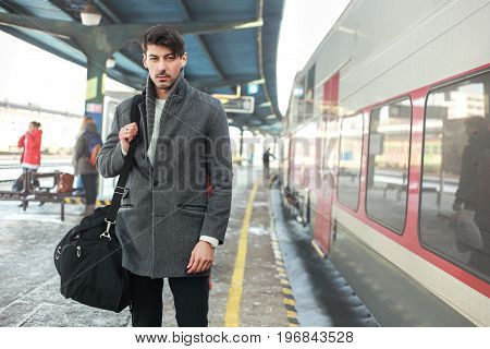 outdoor portrait of young man standing next to the train carrying duffle bag