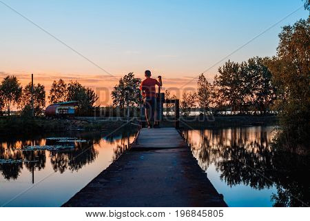 The boy stands on the bridge and admires the sunset over the river.