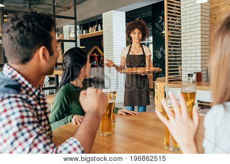 African american woman waitress bringing pizza for clients in cafe