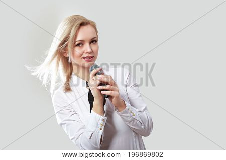 half length portrait of beautiful young woman in white shirt holding microphone in her hand singing satanding next to color background