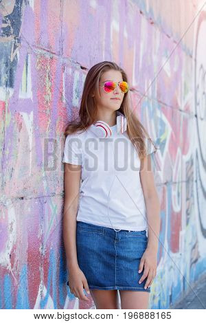 Hipster girl wearing blank white t-shirt, jeans and sunglasses posing against rough street wall, minimalist urban clothing style, mockup for tshirt print store