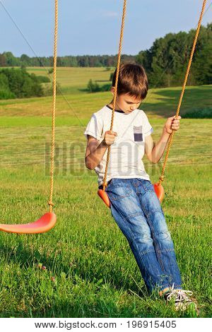 Sad lonely boy sitting on swing alone
