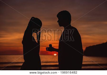 A silhouette man propose marriage to a silhouette woman with sunrise background