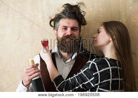 Couple in love hugging with glass and bottle of wine. Happy man or hipster with messy hair smiling with woman or girl on beige wall. Alcohol and convive. Unhealthy lifestyle. Bad habits