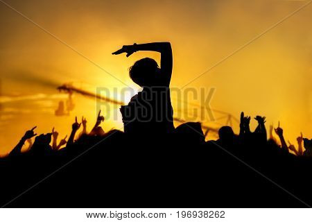 Young girl enjoys a rock concert, Silhouette on sunset, hands up on openair