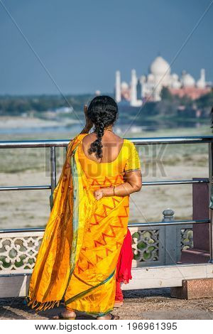Woman in traditional sari shot from the back at Agra Red Fort, a Unesco World Heritage site looking at Taj Mahal in the Indian city of Agra, Uttar Pradesh.