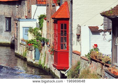 River view to old walls of Bruges buildings. Red bow window over water channel in Bruges.