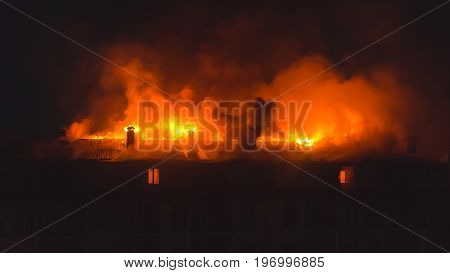 Building in fire at the night burning fire flame with smoke on the apartment house roof.