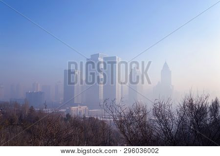 Cityscape Of Winter Urumqi In Smog With Bare Trees Branches In Front