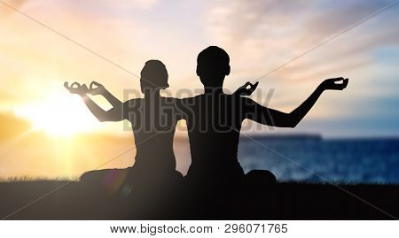 mindfulness, spirituality and outdoor yoga - silhouettes of couple meditating in lotus pose over sunset and sea background