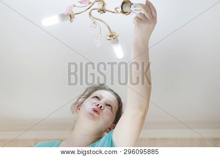 Female Hand Inserts A Light Bulb Into The Threaded Socket. She Is Shining. Installation Of Household