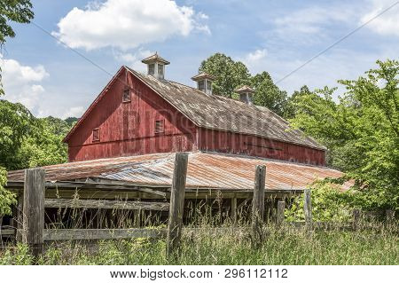 An Old Red Barn, Faded From Its Former Glory, Stands Among Growing Trees And Brush In The Ohio Count