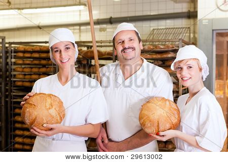 Padeiro fresco de pé com sua equipe na padaria com pão cozido