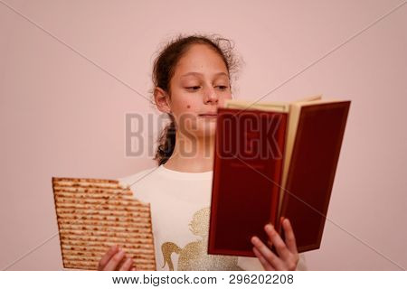 Portrait Of The Cute Teenager Girl Holding Matzah And Reads The Passover Haggadah. Jewish Child Eati