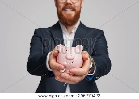 Unrecognizable Businessman With Ginger Beard Demonstrating Piggy Bank With Savings To Camera While S
