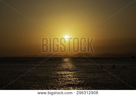 Golden Sunset Over The Sea, Mountain Lines At Background. People Swimming In The Water