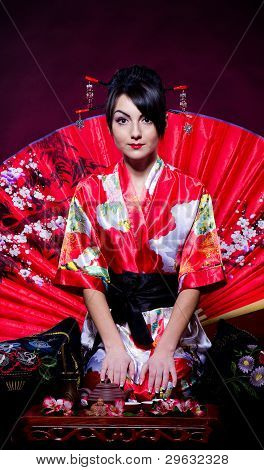Woman in red Asian costume arranging Japanese tea ceremony
