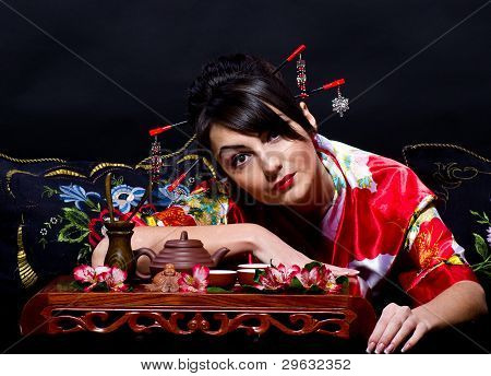 Woman in red Asian costume arranging Japanese tea ceremony