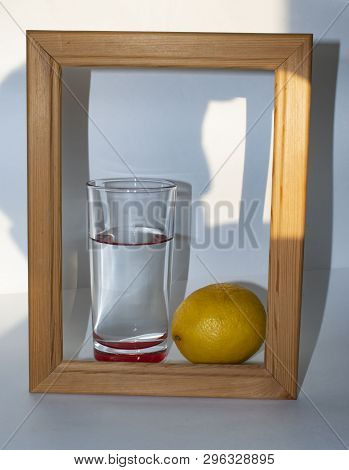 In A Glass Of Pure Clear Water Next To A Lemon In A Wooden Frame On A White Background