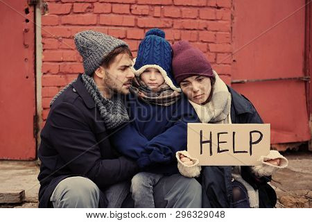 Poor Young Family With Help Sign On Dirty Street