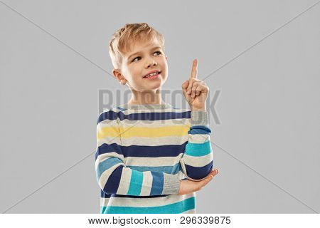 childhood, expressions and people concept - little boy in striped pullover pointing finger up over grey background