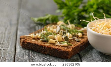 A Piece Of Bread With Bran And Cereals And Sprouted Mung Beans On A Black Table.
