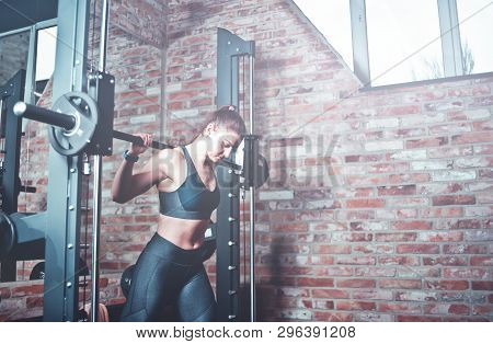 Athletic Young Woman Doing Lunges With The Smith Machine Against Brick Walll With Window At Gym. Ton