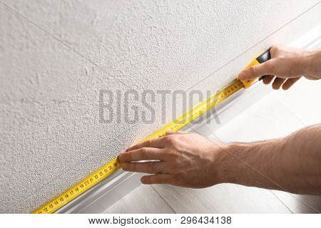 Man Measuring Baseboard Indoors, Closeup. Construction Tool