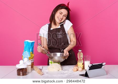 Smiling Inspired Slender Young Lady With Dark Hair Talks Over Mobile Phone, Listening Carefully, Mak