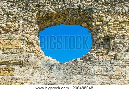 A Hole In The Stone Wall And The Blue Sky In The Background, A Ruined Wall With A Hole. The Image Ca