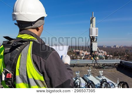 Professional Industrial Climber In Helmet And Uniform Reads Technical Documentation And  Antennas Of