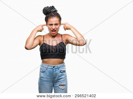 Young braided hair african american with pigmentation blemish birth mark over isolated background covering ears with fingers with annoyed expression for the noise of loud music. Deaf concept.