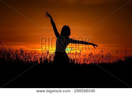 One Young Girl Dancing In A Field Among The Grass, With Her Hands Up, Against A Beautiful Sky With C