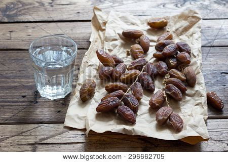 Dried Dates Fruits On A Branch And A Glass Of Water On A Wooden Table. Traditional Fast Breaking, Mu