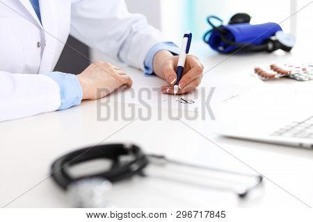 Female Doctor Filling Up Prescription Form While Sitting At The Desk In Hospital Closeup.  Healthcar